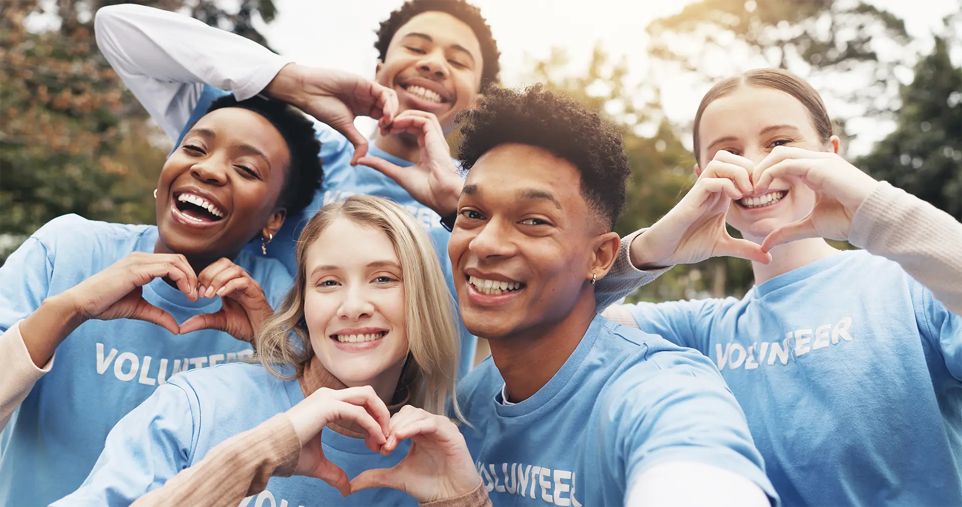 A diverse group of young volunteers forming a heart shape with their hands, symbolizing unity and compassion.